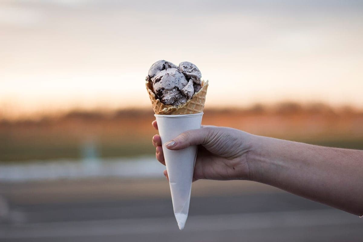 Hand holding a cone of chocolate chip ice cream at sunset