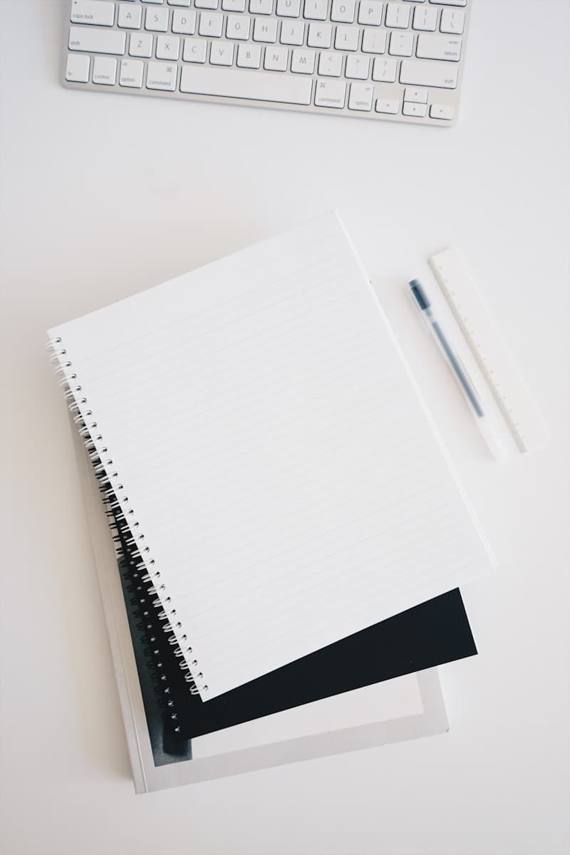 Stack of spiral notebooks beside a keyboard